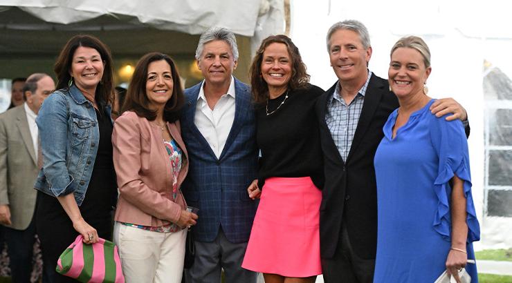 Janis and Jay Beach, Crystal Mintzer, Mark and Charlotte Brainard, and Leslie Mergner all standing closely together in front of an outdoor tent